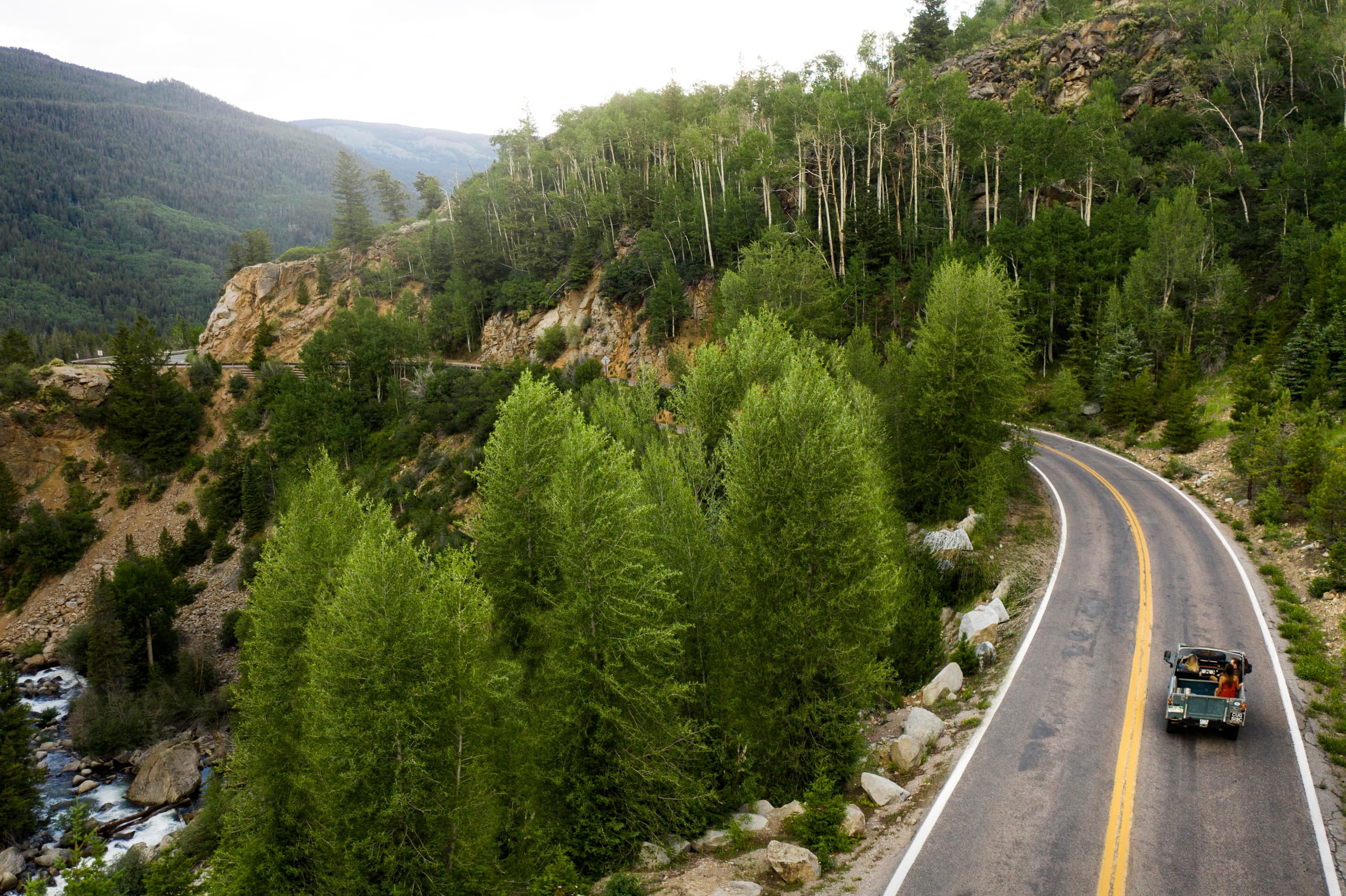 A convoy of two vehicles on an empty road through the highlands, mountains ahead
